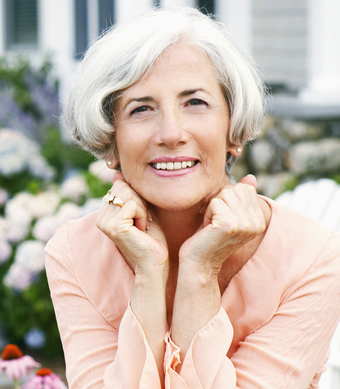 An elderly woman smiling resting her head on her hands in the garden